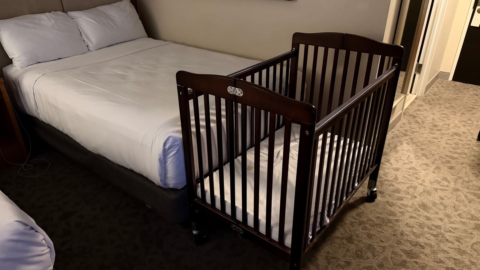 Lit bébé à barreaux installé à côté du lit dans la chambre d’hôtel.